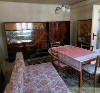 A dining table with a tablecloth and chairs in a simple cabin with wooden furniture.