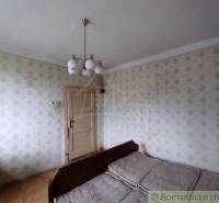 A room in a family house with a bed, vintage wallpaper, and a retro chandelier.