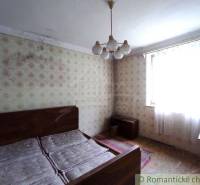 Bedroom in a family house with a double bed, wallpaper, and mold on the wall.