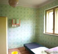 A room in a family house with a simple bed, a wardrobe, and shabby walls.