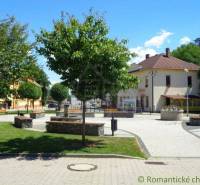 A small square surrounded by trees, benches, and gardens offers a cozy atmosphere for relaxation.