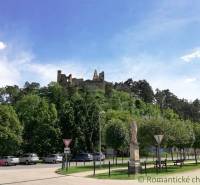 A castle on a hill surrounded by forest and a park with cars in the foreground.