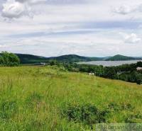 A vast meadow with a view of hills, greenery, and a water reservoir, ideal for gardens.