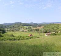 A vast meadow surrounded by hills, with a family house and a village visible in the background.