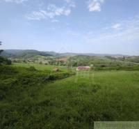 A vast meadow in the valley with a family house surrounded by hills and greenery.