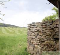 Stone wall, meadow, hills, family house in a natural landscape.