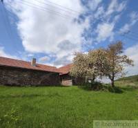 A stone house with trees on a rural property under a bright sky.