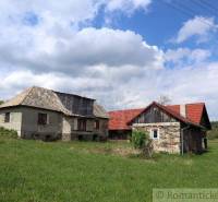 Stone family house with a red roof on a green plot under a blue sky.