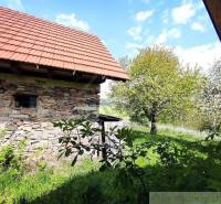 The picture shows a stone family house surrounded by greenery and trees in an idyllic landscape.