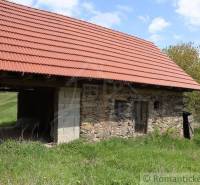 An old stone house, under a red roof, surrounded by nature, offers peaceful living.