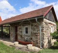A stone family house with a red roof surrounded by a rural landscape and grassy area.