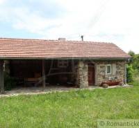 A cottage with stone walls and a tiled roof situated on a spacious green plot.
