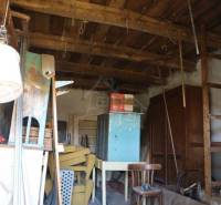 A mess in a wooden shed with old furniture, chairs, and a shelf near the family house.