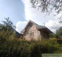 An older family house in the countryside, surrounded by greenery and trees, under a clear blue sky.