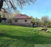 The picture shows a cottage with a garden, trees, and grazing sheep in the countryside.