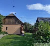 A family house with a garden, a pine tree, and a stone-wooden fence, situated in the countryside.
