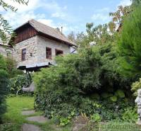 A stone cottage surrounded by a garden with a swing and a statue, creating a romantic atmosphere.