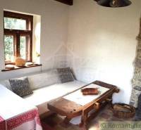 Traditional cottage with a wooden table, sofa on the right, and a stove by the stone wall.