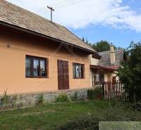In the picture, there is an old cottage with a wooden roof and a stone foundation.