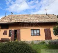 A traditional cottage with wooden shutters and a terracotta roof in a natural setting.