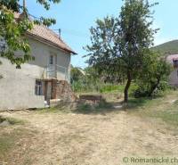 A family house in the countryside with a spacious lawn, trees, and a neighboring building in the background.