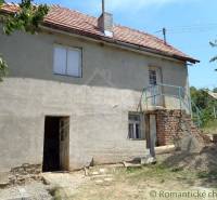 A family house with a simple facade, a garden, and trees in a peaceful rural setting.