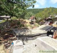 In the picture, there is a garden with a mound of earth, a family house, and a well in the background.