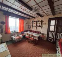 A traditional living room with rustic furniture, orange curtains, and a wooden ceiling, evoking the coziness of a cottage.