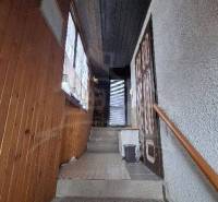 In the picture, there are stairs leading to a door, with wooden wall paneling. Cottage.