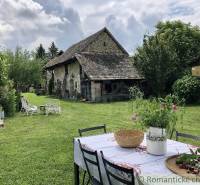 A picturesque garden with a historic cottage, a table, and a family house surrounded by greenery.