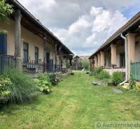 A lawn between traditional houses with verandas and floral decorations. In the background, a wooden shed.