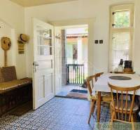 A country kitchen with a wooden table, chairs, and a door leading to the veranda of a family house.