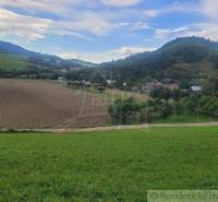 A valley with green fields, fields, trees, and hills in the background under a blue sky.