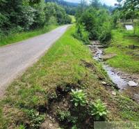 A country road, next to which flows a stream, surrounded by agricultural and forest land.