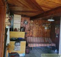 The interior of a cottage with a wooden wall, a couch, and a traditional tiled stove in a family house.