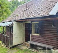 An old family house, wooden walls, sloped roof, small shelter, green surroundings.