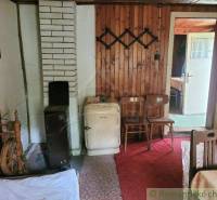 The interior of a traditional cottage with wooden walls, an old stove, and a tiled stove.