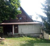 A cabin surrounded by trees in a natural setting with a wooden porch and a satellite dish.