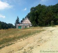 A cottage in the middle of nature surrounded by grassy slopes and forests.