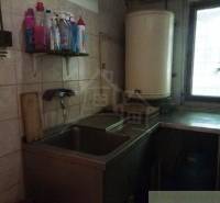 A kitchen with a sink in a cottage, cleaning products on the shelf.