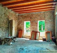 Stone walls, wooden ceiling, and windows prepare the space in the family house for renovation.