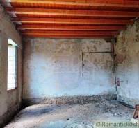 Unfinished interior of a family house, exposed wooden ceilings, old plaster, light penetrating through the windows.
