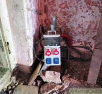 An electrical distribution box in the corner of a family house room, surrounded by stones and a wall.