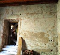 The dilapidated interior of an old family house with an exposed brick wall and wooden planks.