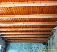A wooden beam ceiling in a family house, with plastered walls and exposed bricks.