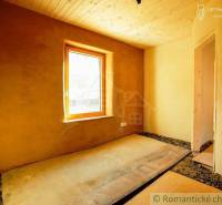 Interior of a room with a wooden ceiling, clay walls, a window, and a floor made of OSB boards.