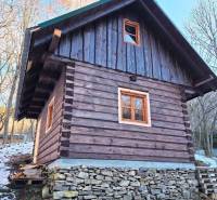 A wooden cabin stands on stone foundations in the middle of nature with the first signs of snow.