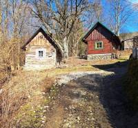 Wooden cottages amidst nature, bordered by trees and a rocky path, in a tranquil area.