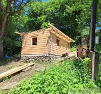 A wooden cabin on a construction site, surrounded by forest, with steep green terrain, ideal for relaxation.