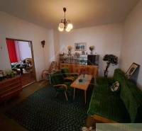 Living room with a green armchair, retro sofa, display cabinet, and flowers in a family house.